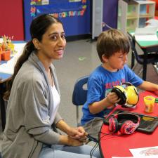 Female Education Assistant sits with elementary school boy, playing with playdough