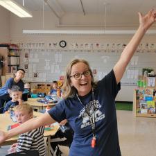 Teacher happy with arms held wide open in her classroom.